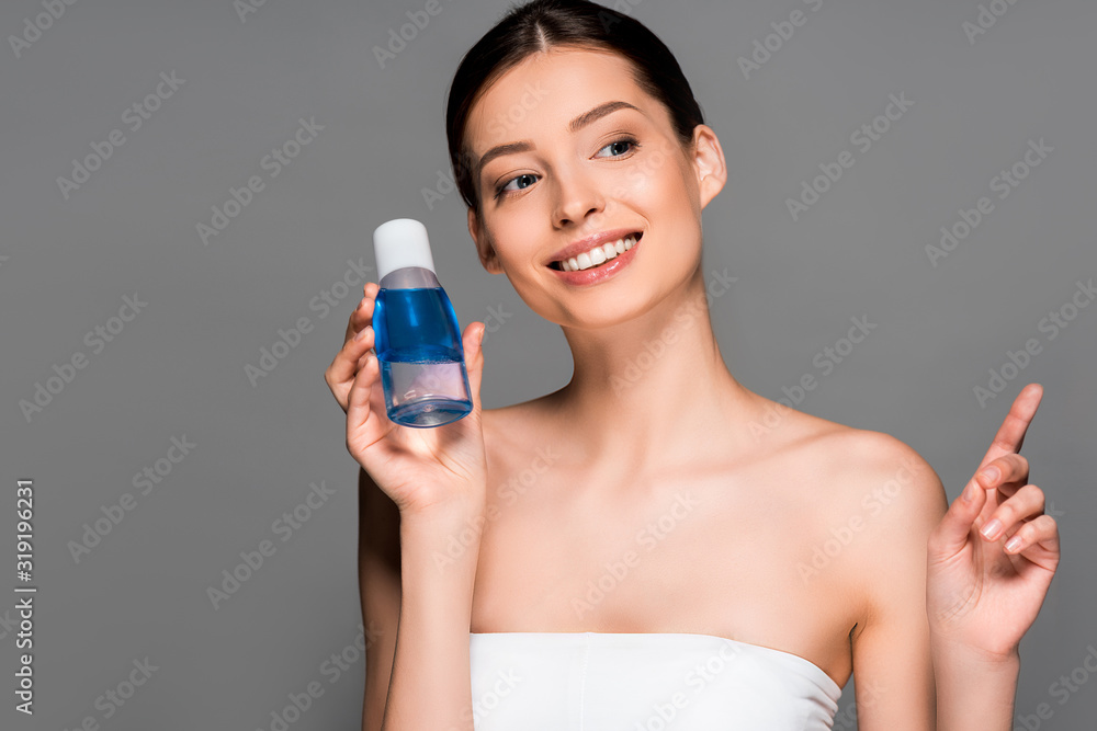 portrait of smiling woman holding bottle of makeup remover, isolated on grey portrait of smiling woman holding bottle of makeup remover, isolated on grey