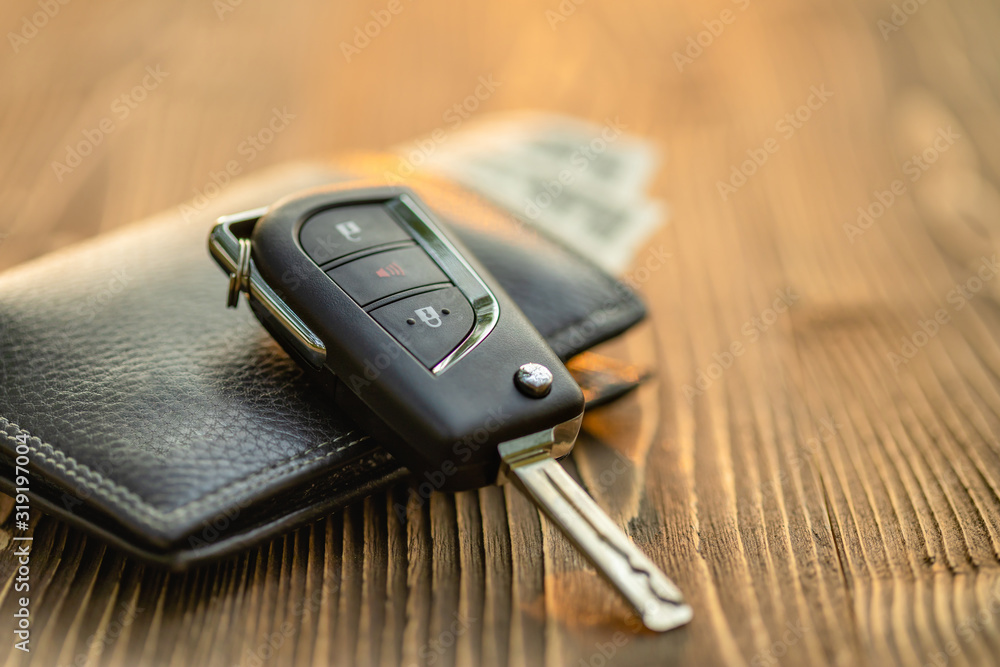 New car keys with US dollar banknote on wooden table. Car purchase or car rental concept New car keys with US dollar banknote on wooden table. Car purchase or car rental concept