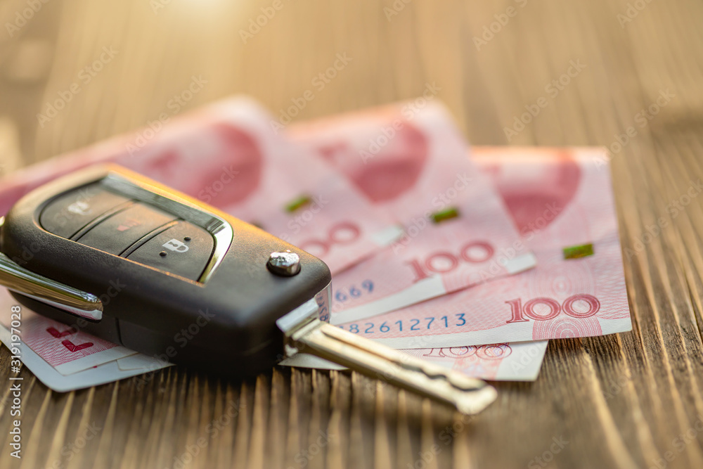 Fototapeta premium New car keys with Chinese banknote on wooden table. Car purchase or car rental concept.
