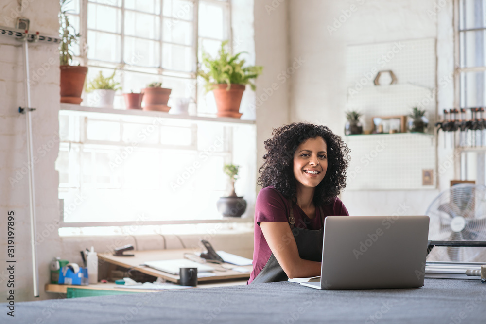 Smiling young woman using a laptop in her framing shop Smiling young woman using a laptop in her framing shop