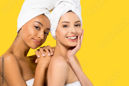 portrait of smiling multiethnic girls with towels on heads, isolated on yellow
