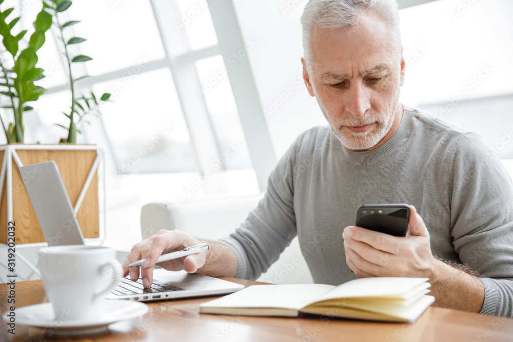 Photo of serious mature man working with laptop and cellphone Photo of serious mature man working with laptop and cellphone