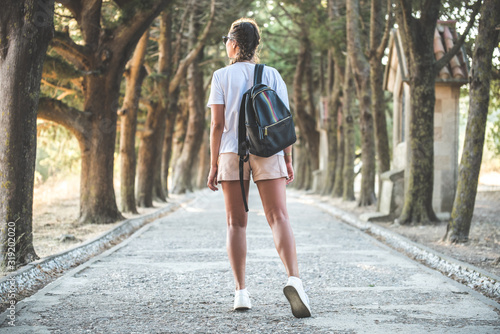 A slender girl traveler with a backpack walks along the alley.