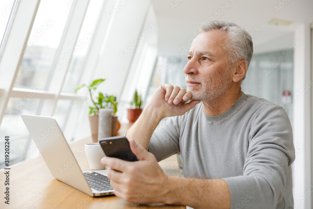 Photo of serious mature man working with laptop and cellphone Photo of serious mature man working with laptop and cellphone