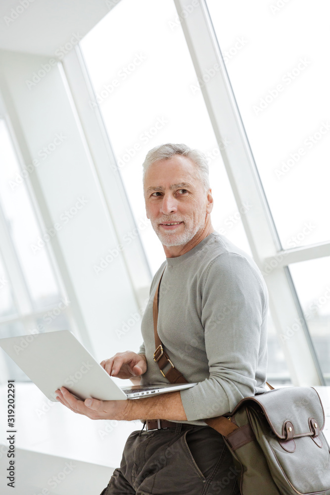 Photo of pleased gray-haired man holding and using laptop Photo of pleased gray-haired man holding and using laptop