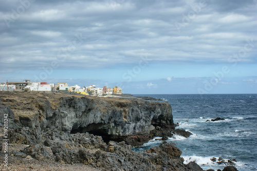 A small picturesque village (Las Eras) on a rocky shore. Waves break on the shore in cloudy weather.