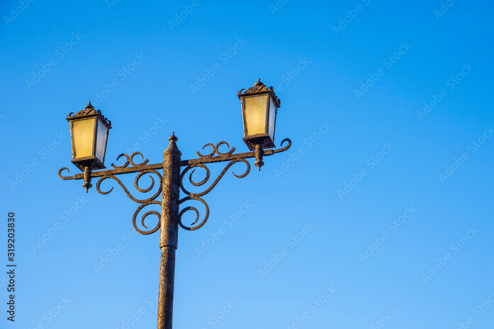 Two street lights against the blue sky.