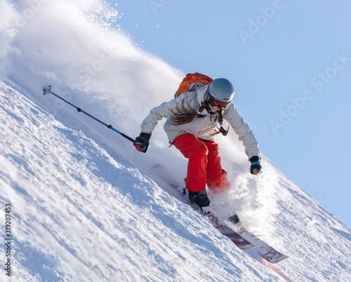 Girl On the Ski. a skier in a bright suit and outfit with long pigtails on her head rides on the track with swirls of fresh snow. Active winter holidays, skiing downhill in sunny day. Woman skier