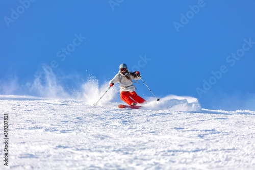 Girl On the Ski. a skier in a bright suit and outfit with long pigtails on her head rides on the track with swirls of fresh snow. Active winter holidays, skiing downhill in sunny day. Woman skier