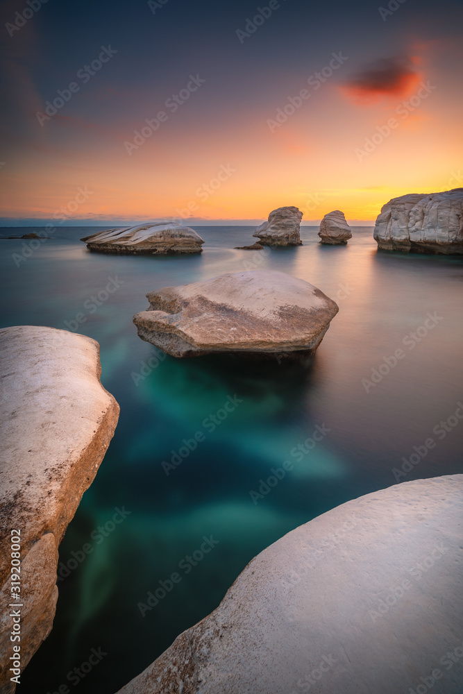 Beautiful sunset at the rocky beach near Limassol Cyprus with smooth water and white rocks standing out of water - obrazy, fototapety, plakaty 