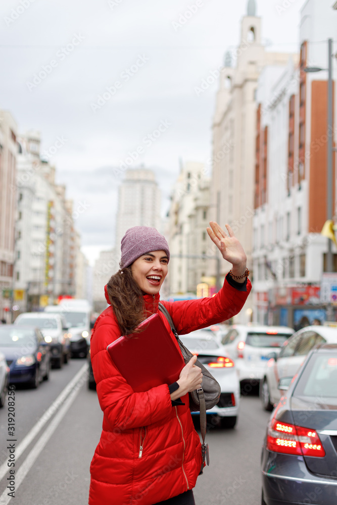 Smiling young woman waving to someone as she crosses a downtown street