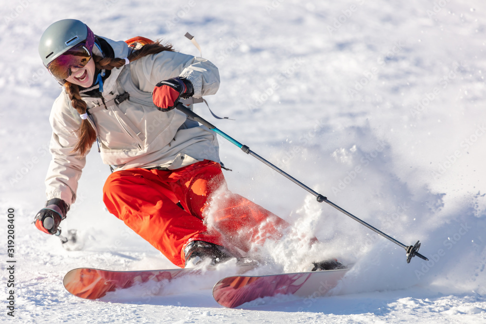 Girl On the Ski. a skier in a bright suit and outfit with long pigtails on her head rides on the track with swirls of fresh snow. Active winter holidays, skiing downhill in sunny day. Woman skier - obrazy, fototapety, plakaty 