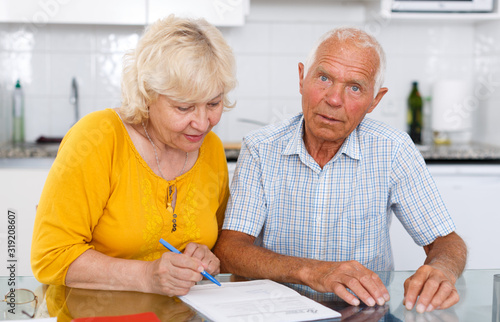 Smiling mature couple in home interior filling up documents