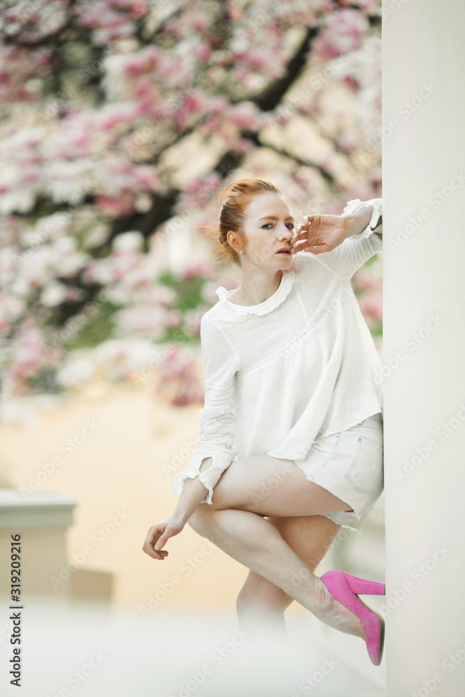 Girl in the stylish outlook stands on the flowering tree background Girl in the stylish outlook stands on the flowering tree background