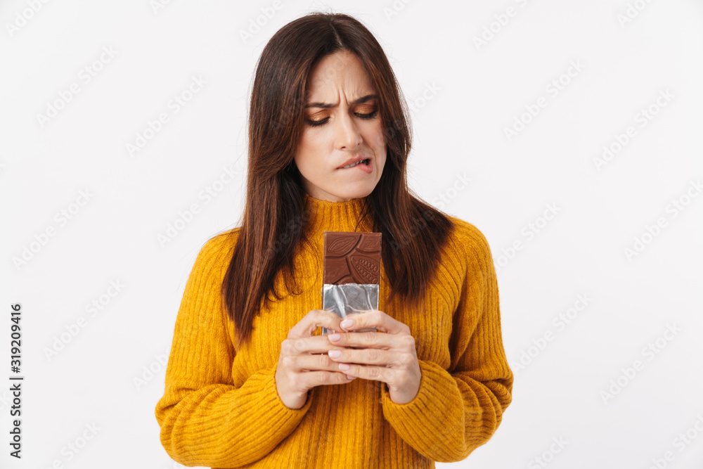 Image of beautiful adult woman hesitating while holding chocolate bar