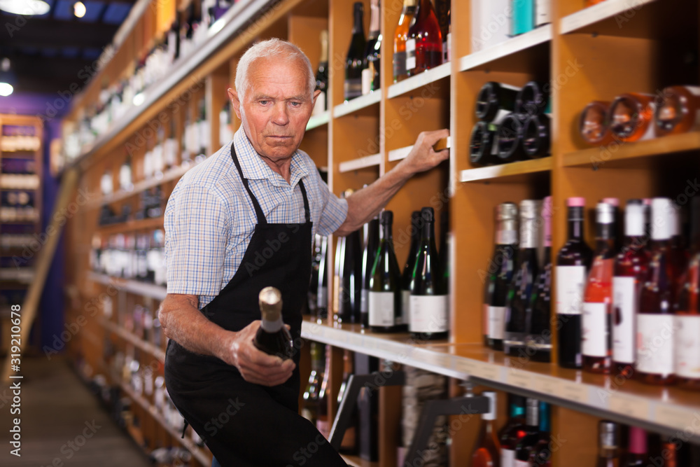 Mature male vintner holding out bottle of wine