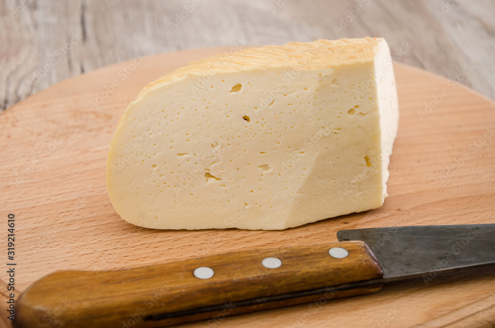 piece of hard cheese on a wooden background and a knife. Ukrainian cheese.
