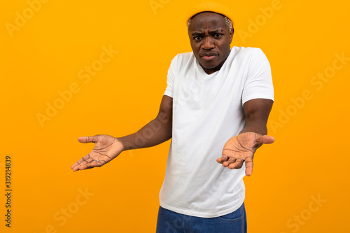 charismatic african man in a white t-shirt with a layout outraged in surprise on a yellow studio background