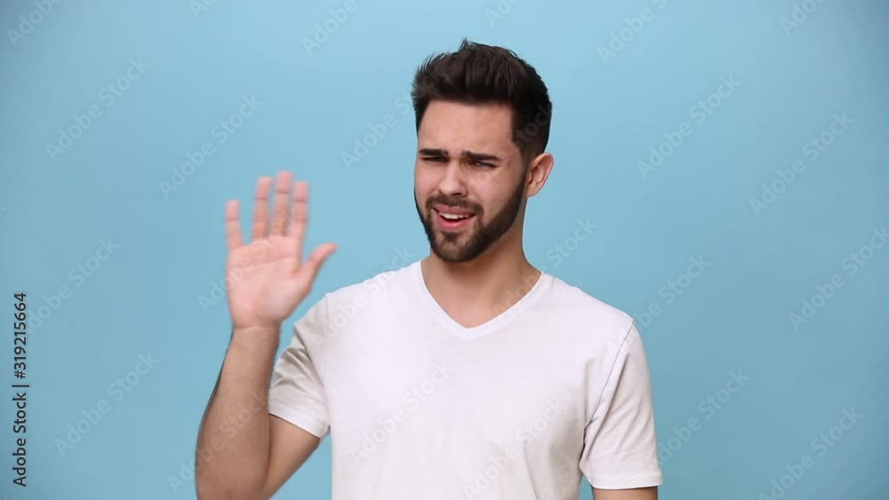 Handsome unshaven bearded young guy 20s wearing white t-shirt isolated on pastel blue background in studio. People sincere emotions lifestyle concept Looking at camera showing no gesture say not agree Handsome unshaven bearded young guy 20s wearing white t-shirt isolated on pastel blue background in studio. People sincere emotions lifestyle concept Looking at camera showing no gesture say not agree