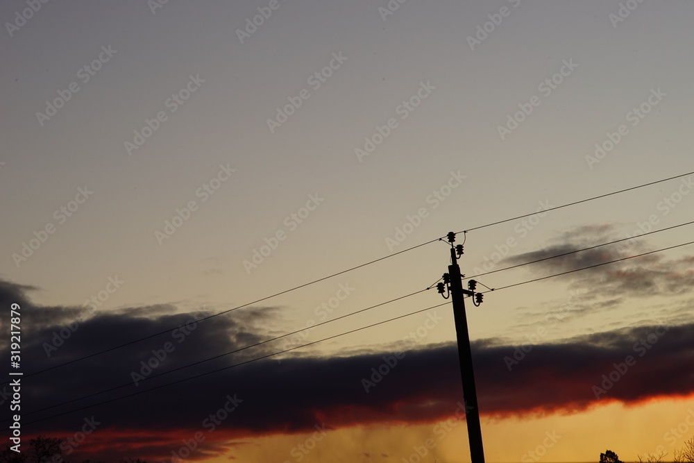 Silhouette high voltage electric tower in dark sunset sky.