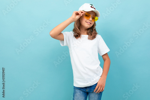 Cool caucasian teenager girl in white t-shirt, yellow glasses smiles and shows herself isolated on blue background