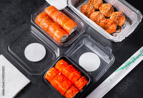 boxes with rolls California with salmon, Philadelphia with caviar, baked rolls with cream sauce and sesame on a black background close-up, sticks, napkins
