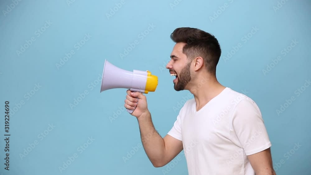 Unshaven bearded young guy 20s wearing white t-shirt isolated on pastel blue background in studio. People sincere emotions lifestyle concept. Side scream in megaphone announces discounts sale Hurry up Unshaven bearded young guy 20s wearing white t-shirt isolated on pastel blue background in studio. People sincere emotions lifestyle concept. Side scream in megaphone announces discounts sale Hurry up