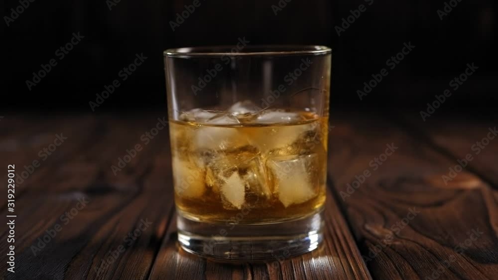 Glass of whiskey with ice on wooden table. Copy space. A glass of whiskey with ice on a wooden background in the dark with artificial lighting. Glass of whiskey with ice on wooden table. Copy space. A glass of whiskey with ice on a wooden background in the dark with artificial lighting.