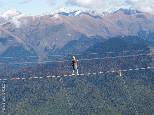 A girl walks on a suspension bridge over a precipice against the backdrop of a mountain range