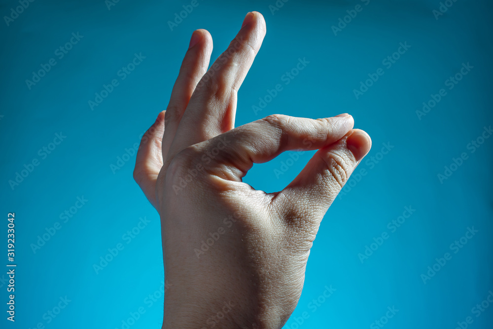 male hand shows ok finger sign on blue background copy space close up