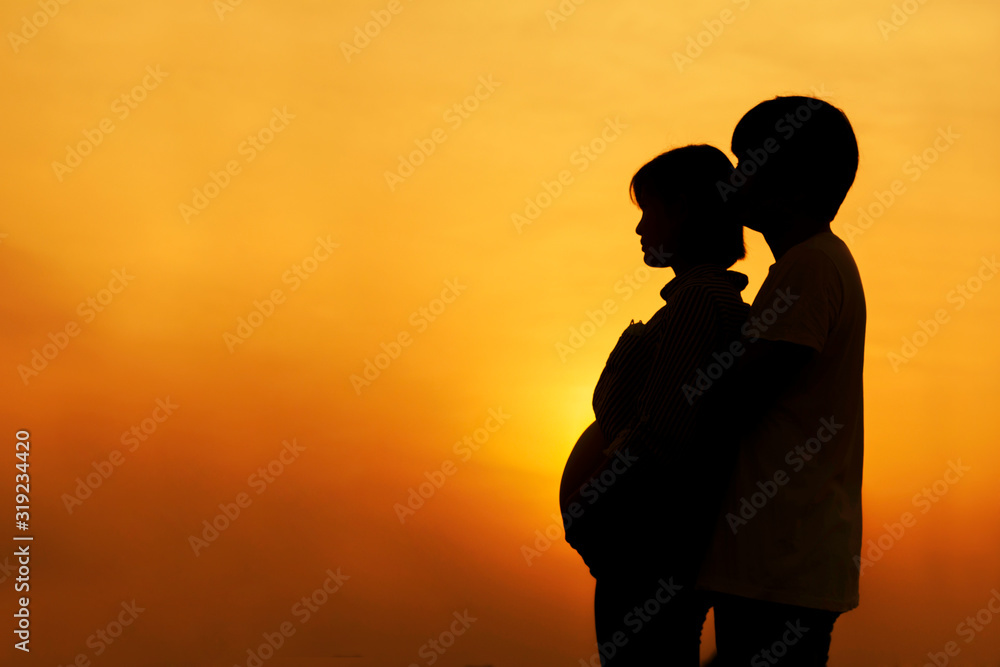Silhouette of a couple Pregnant couple hug and holding belly talking with their child on sunset background.