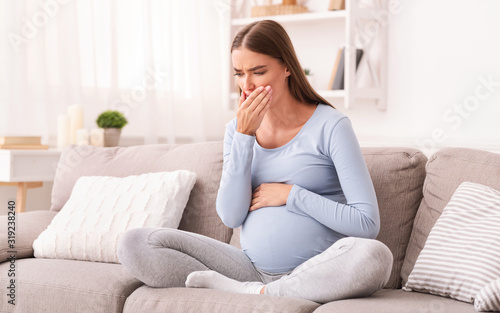 Pregnant Girl Touching Mouth Sitting On Couch Indoor