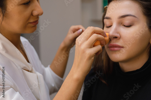 Make-up artist in the process of creating trendy nude makeup. Girls of Caucasian appearance with long hair and well-groomed looks