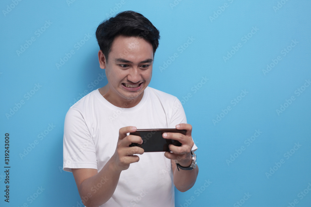 Funny Young Asian Guy Playing Games on Tablet Smart Phone Funny Young Asian Guy Playing Games on Tablet Smart Phone