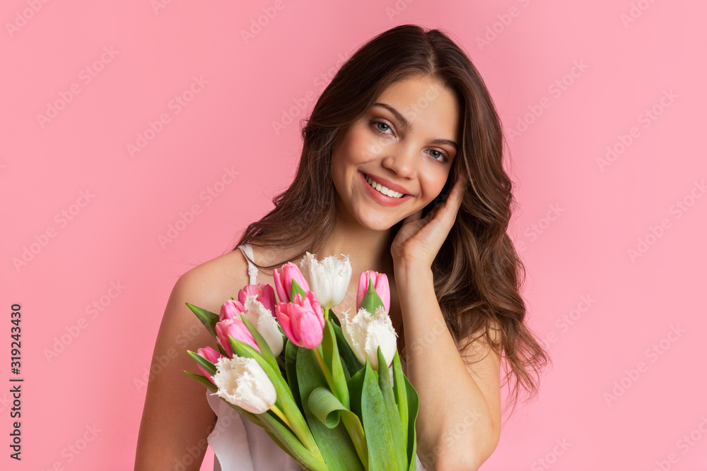 Beautiful smiling girl holding bouquet of tulips, posing over pink background