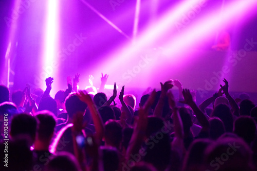 Blurred image of silhouette of raised arms, crowd of people in the front of bright stage lights at concert
