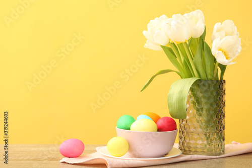 Easter eggs in a basket and flowers on the table. Festive easter background with place to insert text.