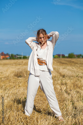 Young beautiful blonde woman in a beige suit posing against the background of a mowed wheat field