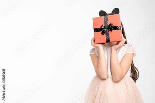 Young girl in beige dress vovered her face with red gift box isolated over white background, copyspace for your text photo