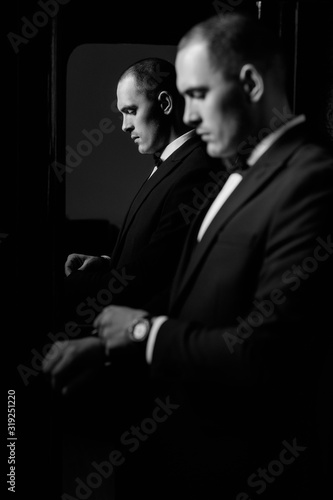 Sexy fashionable man in tuxedo indoor. Close up of a concerned groom to the side while wearing tuxedo and bow tie, standing. Fees groom in the room. Black and white photo