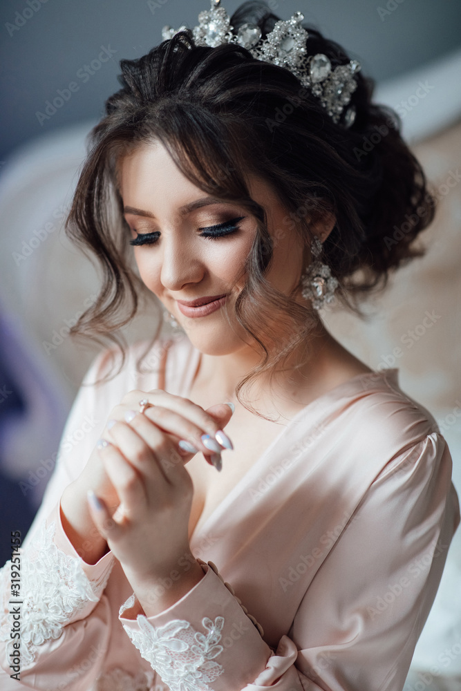 Beautiful brunette Bride portrait wedding makeup and hairstyle with diamond crown, fashion bride model jewelry and beauty female face, gorgeous beauty bride, bride in luxury robe. The bride sits in be