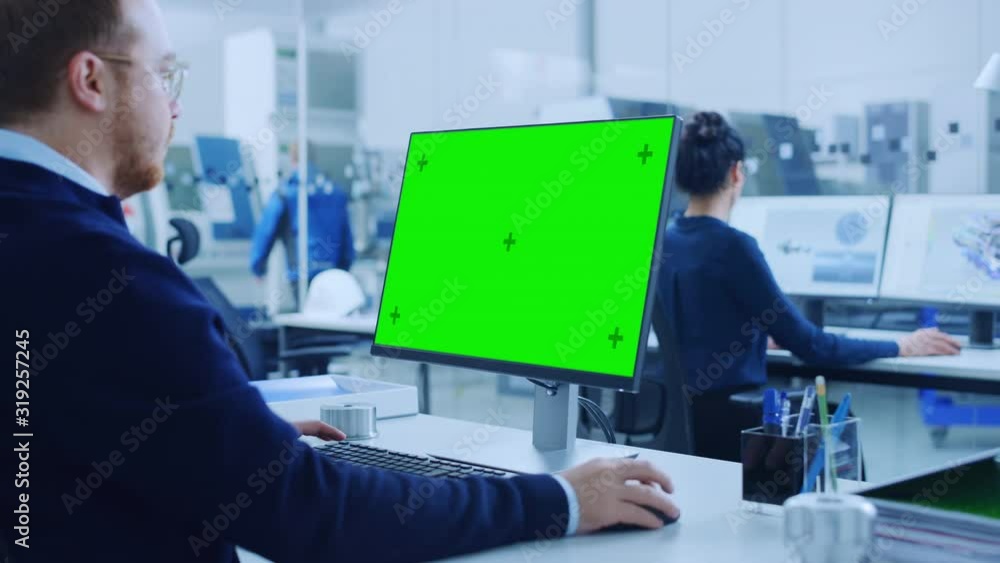 Over the Shoulder: Heavy Industry Engineer Working on Personal Computer, Display is Green Mock-up Screen or Chroma Key. Industrial Factory with High-Tech CNC Machinery, Professionals Working Over the Shoulder: Heavy Industry Engineer Working on Personal Computer, Display is Green Mock-up Screen or Chroma Key. Industrial Factory with High-Tech CNC Machinery, Professionals Working