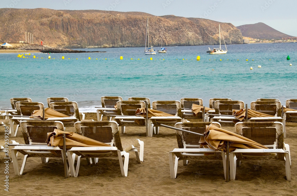Sunbeds on Playa de Las Vistas beach in Tenerife,Canary Islands,Spain. Travel or vacation concept.Selective focus. Sunbeds on Playa de Las Vistas beach in Tenerife,Canary Islands,Spain. Travel or vacation concept.Selective focus.