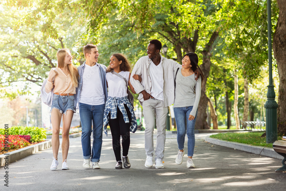 Students walking in park after university, chatting and having fun Students walking in park after university, chatting and having fun