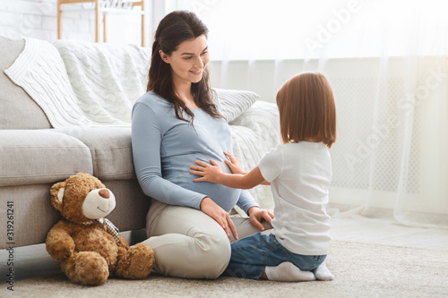 Curious little girl touching her pregnant mother big belly photo