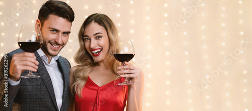 Young Couple Posing With Red Wine Glasses Over Beige Background