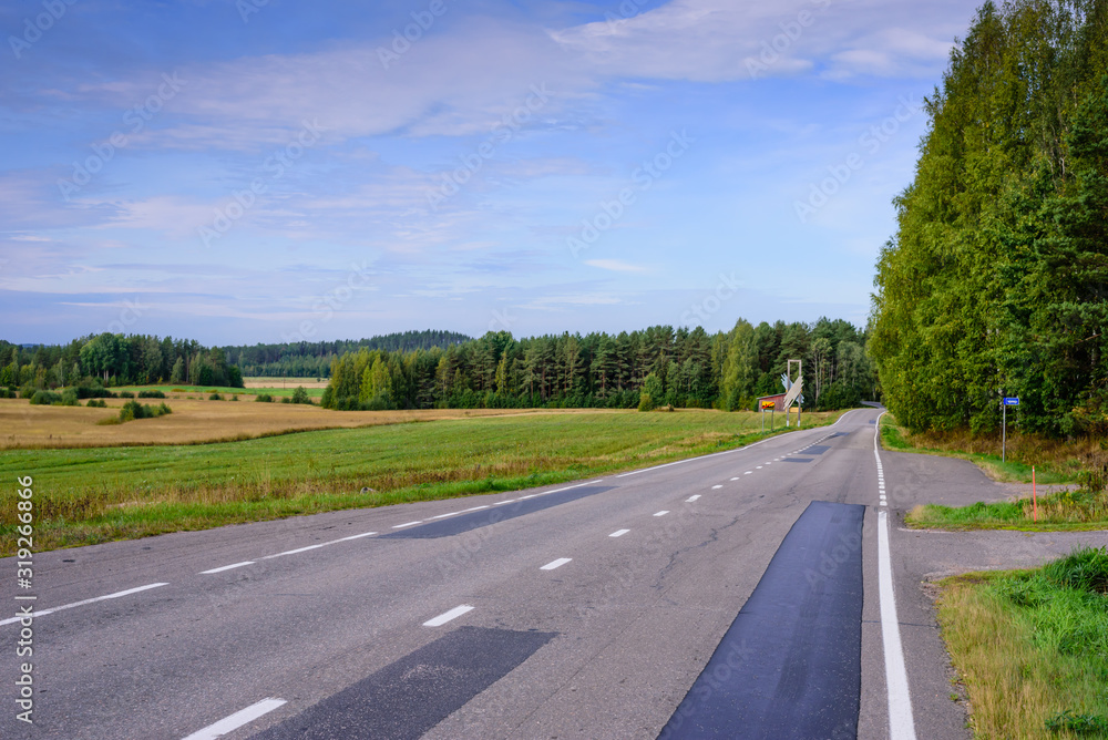 Asphalt road on the background of blue sky with clouds. Typical landscape of Finland Asphalt road on the background of blue sky with clouds. Typical landscape of Finland