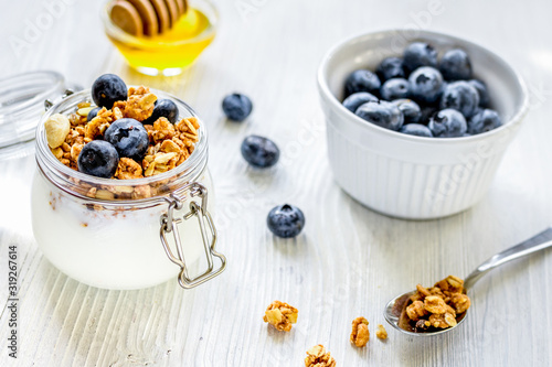Homemade granola with blueberries in jar on white kitchen background