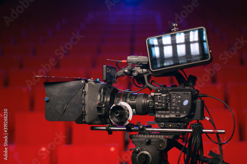 Professional video camera in a movie theater with red seats and blue light projector