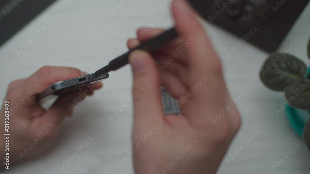 Man hands repairing smartphone by small portable screwdriver on white wooden table, top view